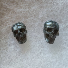 Load image into Gallery viewer, A close of of grey colored skull stud earrings that shimmer silvery in the light.