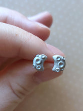 Load image into Gallery viewer, A pair of silver metallic crescent moons with 3D craters on the surface held between finger and thumb.