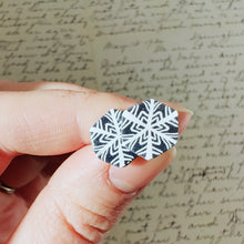 Load image into Gallery viewer, Two hexagon shaped earrings with a snowflake pattern in silver and white. The earrings are held in bright sunlight and have small silver sparkles in the grey areas. 
