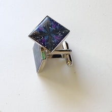 Load image into Gallery viewer, A pair of silver colored cufflinks with a bezel on top. The bezel is filled with polymer clay with a shiny gloss finish. The clay is dark blue with veins of gold, purple, and glow in the dark clay radiating from the center. 
